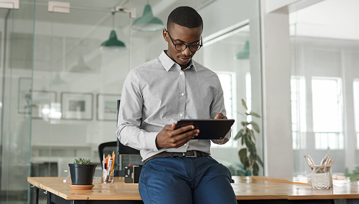 African American man leaning on desk and using tablet